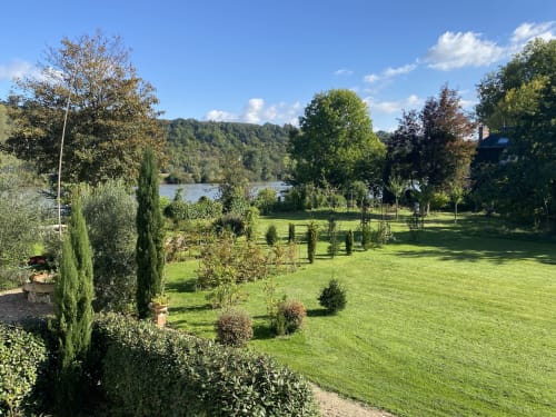 Lush garden grounds at Clairseine cottage with river view, manicured lawn, cypress trees, and Seine waterfront beyond.