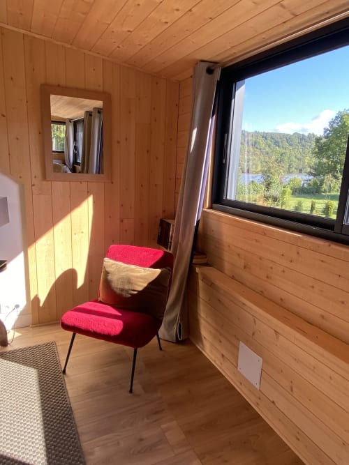 Cozy wooden cottage interior at Clairseine B&B with red chair, river view window, and natural light in The Nest room