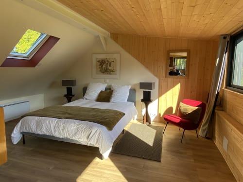 Bright attic bedroom at Clairseine B&B with wood beams, skylight, queen bed, red chair, and river views near