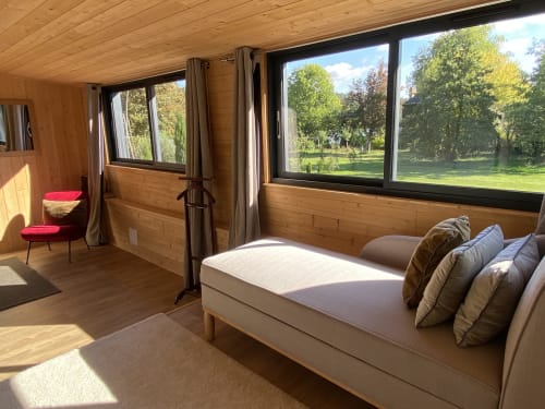 Wooden cottage bedroom at Clairseine with river views, queen bed, pink chair, and large windows overlooking gardens at