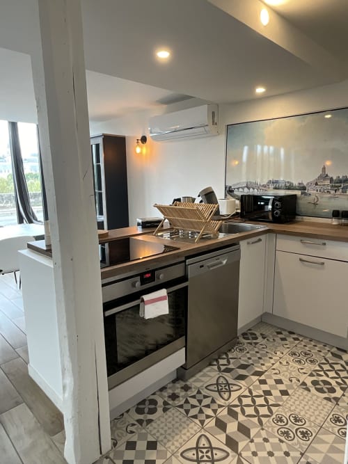 Modern kitchen in Gîte Le Relais Viennois, Blois with stainless steel appliances, white cabinets, patterned tiles, and river