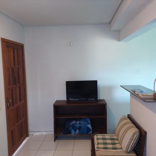Apartamento aconchegante na Pousada Serra Azul em Juquiá com TV, móveis de madeira e poltrona listrada em piso de azulejo
