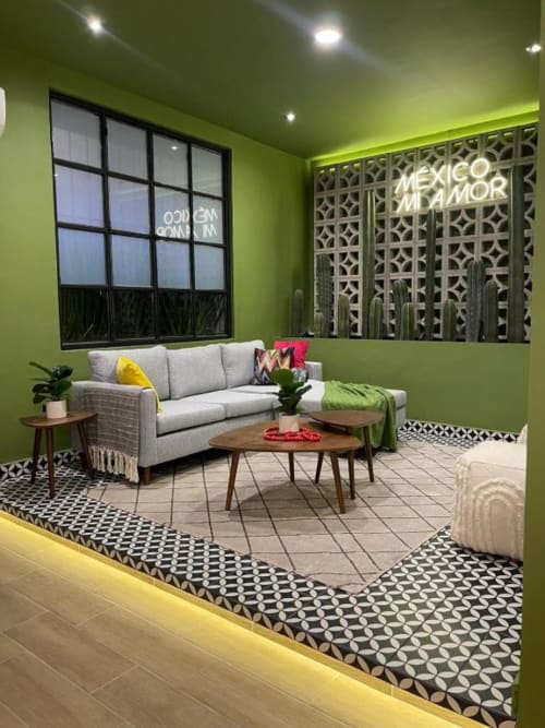 Sala de estar verde vibrante en Casa Donceles Mexico City con sofá gris seccional, mesas de madera y piso con patrón geométrico