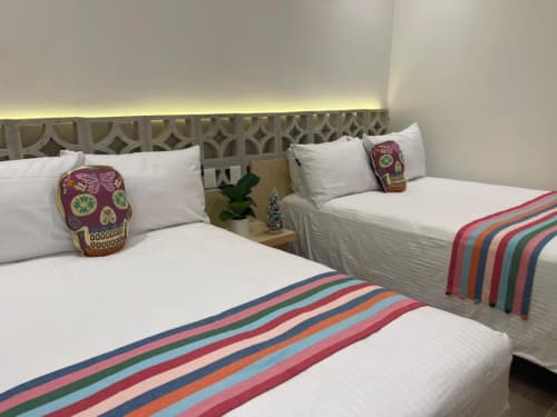 Habitación de hotel luminosa con dos camas, mantas a rayas coloridas, almohadas con calaveras decorativas y cabecera geométrica en Casa