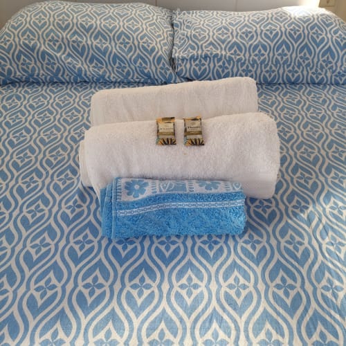 Toalhas brancas e azuis arrumadas cuidadosamente com itens de higiene cortesia sobre cama estampada azul na Pousada Serra Azul, Juquiá