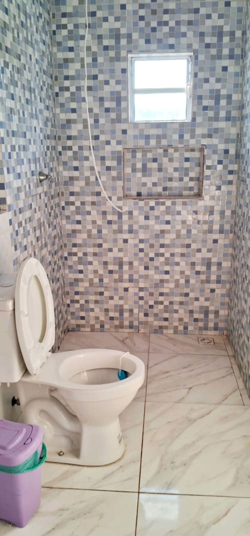 Banheiro com azulejos de mosaico azul, vaso sanitário branco, piso de mármore e janela na Pousada Serra Azul em Juquiá