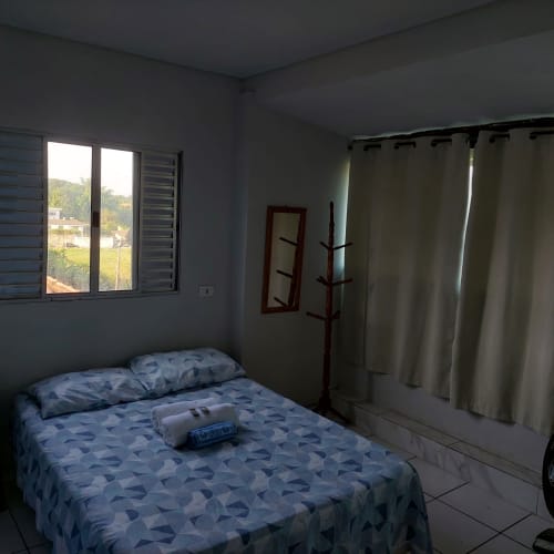 Quarto da Pousada Serra Azul em Juquiá com vista para as montanhas, cama com roupa de cama estampada azul, espelho de madeira e cabideiro