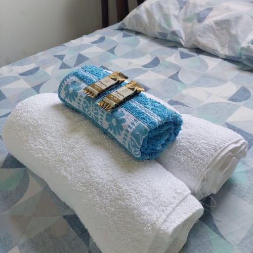 Toalhas enroladas com detalhes dourados sobre a cama na Pousada Serra Azul, apartamento com vista para a serra de Juquiá