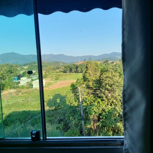 Vista do vale da serra pela janela da Pousada Serra Azul, com campos verdes e morros em Juquiá