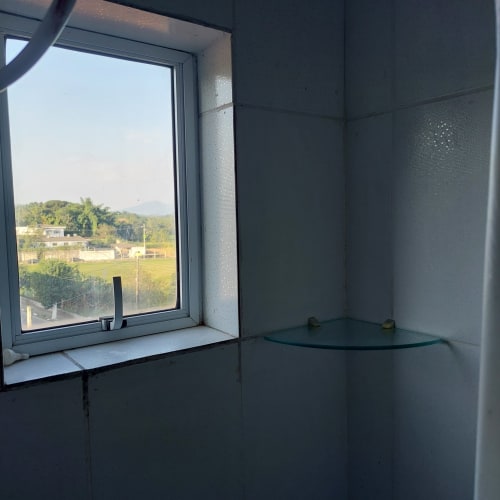 Janela do quarto na Pousada Serra Azul em Juquiá com vista para as montanhas, campos verdes e paisagem rural