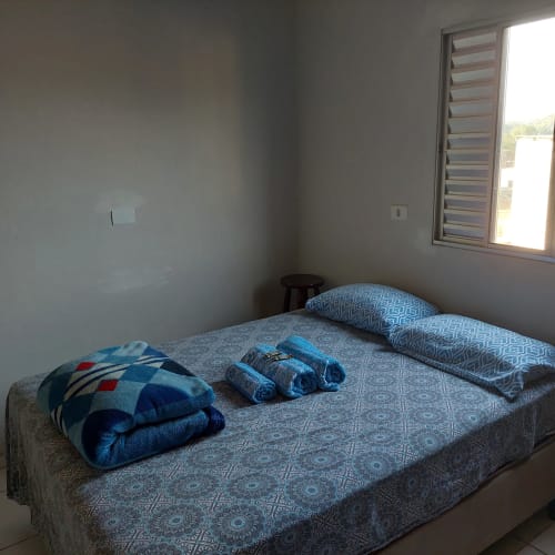 Quarto da Pousada Serra Azul em Juquiá com cama, almofadas azuis, toalhas e janela com veneziana