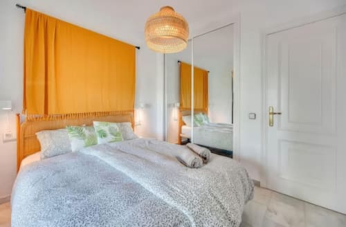 Dormitorio luminoso en apartamento SACORO en Marbella con cama dosel naranja, espejo, lámpara colgante tejida y puertas blancas modernas