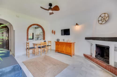 Sala de estar de apartamento moderno en Marbella con chimenea, comedor, muebles de madera y ventilador de techo
