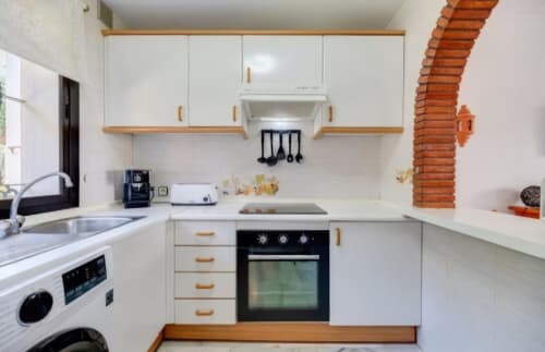 Cocina moderna blanca con tiradores de madera, horno negro y electrodomésticos de acero inoxidable en apartamento SACORO, Marbella