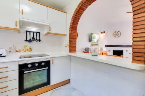 Cocina moderna con muebles blancos, detalles de madera, arco de ladrillo y horno negro en apartamento SACORO, Marbella