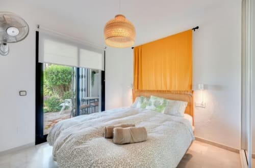 Dormitorio moderno en apartamento SACORO de Marbella con cama dosel naranja, lámpara colgante tejida y puertas con vistas al jardín
