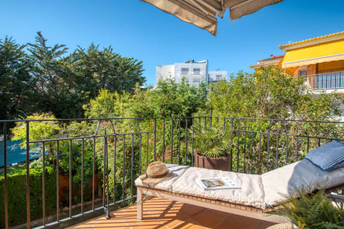 Terraza soleada en Finques Garcia Enrich en Palafrugell con tumbonas, sombrero, revista y vistas al mar entre la vegetación