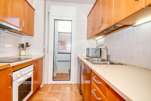 Cocina de galera moderna con gabinetes de madera, electrodomésticos blancos y piso de terracota en Finques Garcia Enrich en Palafrugell
