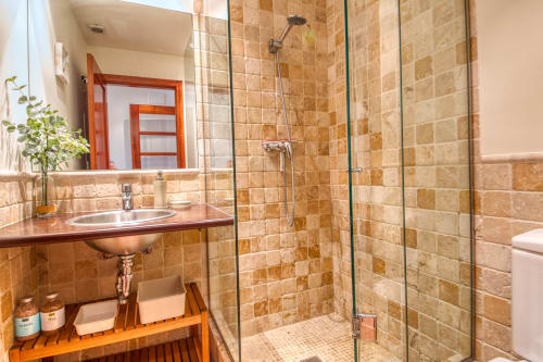 Cuarto de baño de lujo en Finques Garcia Enrich con azulejos de travertino, ducha de cristal, tocador de madera y espejo en Palafrugell