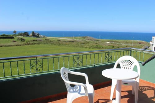 Terraza con vistas al océano en Apartamentos Los Gemelos en Foz, amueblada en blanco con vistas a acantilados verdes y la costa atlántica azul