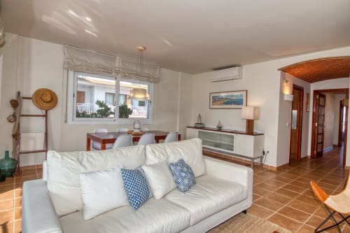 Bright living room in Calella apartment with white sofa, wooden floors, dining area, and garden view through windows