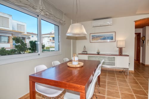 Modern dining room in Calella apartment with wooden table, white chairs, pendant light, and garden views through large