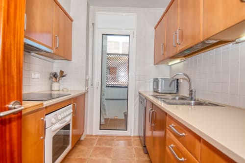 Modern kitchen with orange cabinetry, white tile backsplash, stainless steel appliances, and door to balcony in Calella