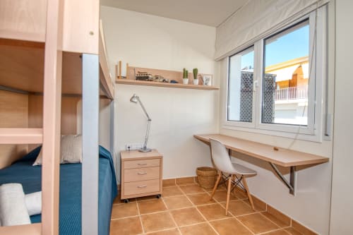 Bright bedroom in Calella apartment with loft bed, wooden desk, chair, and large window overlooking garden