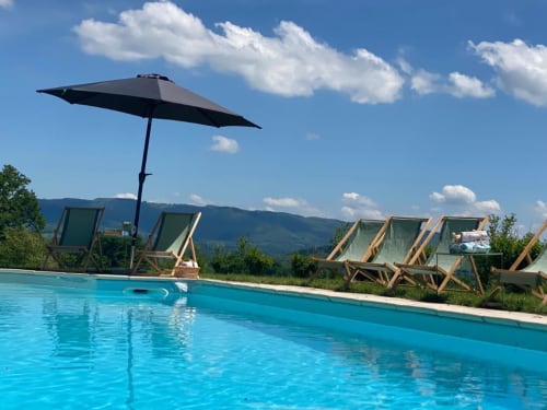 Turquoise pool with black umbrella and deck chairs at Château de Vaux Morlan, Étang sur Arroux, mountains in background