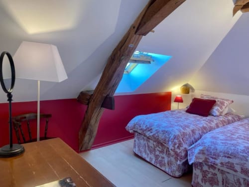 Attic bedroom at Château de Vaux Morvan with two beds, red walls, exposed beam, and skylight window
