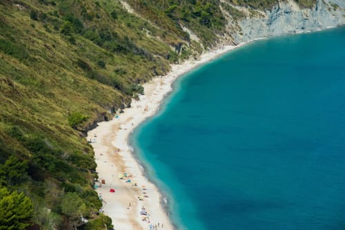 Vista aerea della spiaggia del Mare Adriatico turchese con sabbia bianca, scogliere verdi e bagnanti presso Marcelli, costa del Conero