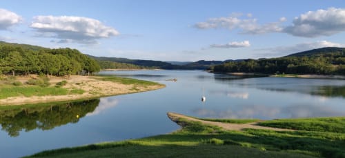 Vue pittoresque du lac avec collines boisées, plages de sable et voilier près des gîtes de Flo, Saint Ennemond