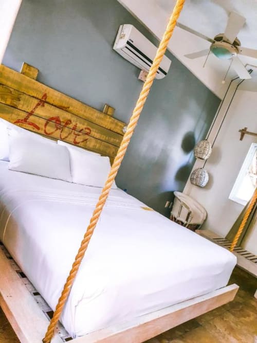 Habitación del Hotel 40 Cañones en Mahahual con cama blanca, columpio de cuerda amarilla y pared verde salvia