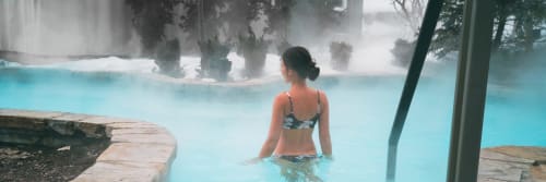Woman in geothermal pool at Brides-les-Bains spa resort with misty hot springs and forest backdrop