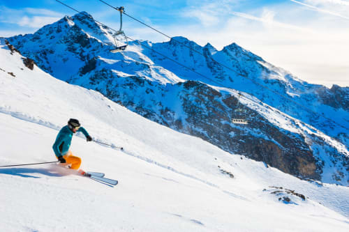 Skier descending snowy slope with snow-covered mountains and ski lift at Brides-les-Bains resort