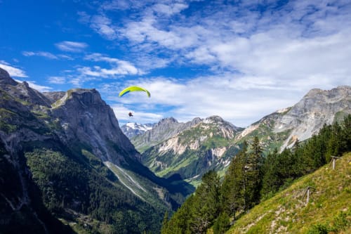 Parapentiste survolant la vallée alpine près de Brides-les-Bains avec pics rocheux spectaculaires et forêts verdoyantes