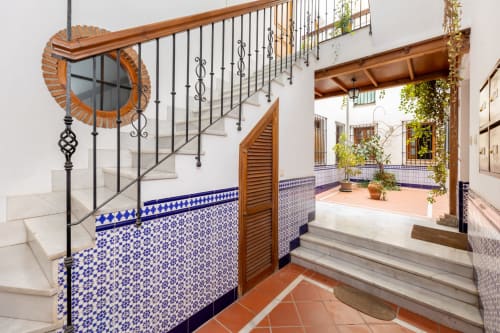 Entrada de un patio andaluz con escaleras de mármol, barandilla de hierro forjado y azulejos decorativos azules