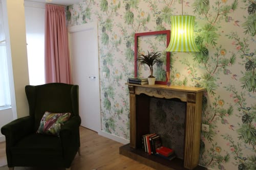 Rincón decorativo con sillón verde, chimenea vintage, papel floral y lámpara colgante con detalles vibrantes en Granada.