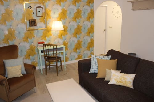 Salón moderno con sofá marrón, sillón a juego, pared floral, mesa de centro blanca, cuadros decorativos y lámpara en Granada.