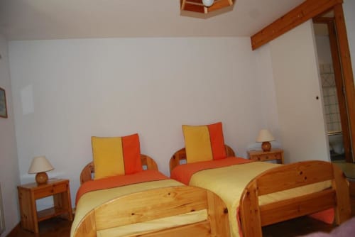 Chambre lumineuse aux Chambres d'hôtes le Grand Bienfaisy avec deux lits en bois, literie rouge et jaune, tables de nuit en bois