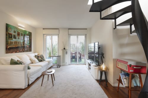 Appartamento moderno a Milano in GIRESIO 41 con divano color crema, porte in vetro verso il balcone, scala a spirale e arredamento minimalista