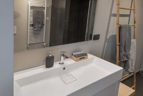 Bagno moderno alla GIRESIO 41 Milan B&B con lavabo bianco, specchio, asciugamani grigi e scaletta in legno