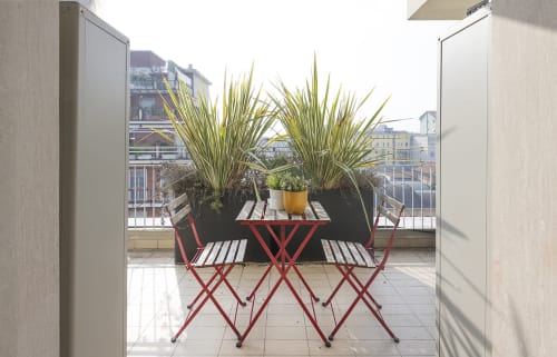 Sedie rosse da café e palme in vaso sul balcone di GIRESIO 41 Milano con vista sulla città