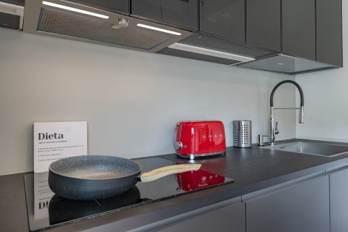 Moderno bancone da cucina nella struttura GIRESIO 41 Milano con bollitore rosso, padella e utensili su piano scuro