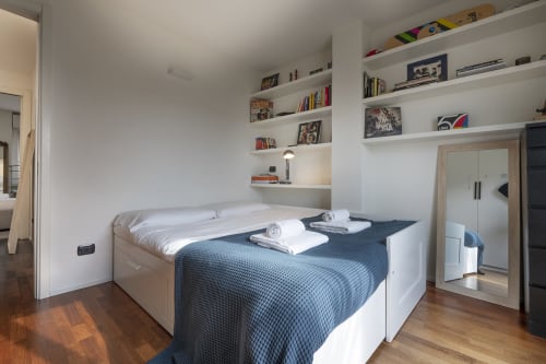 Camera da letto moderna del B&B di Milano con librerie bianche in nicchia, copriletto blu, pavimenti in legno