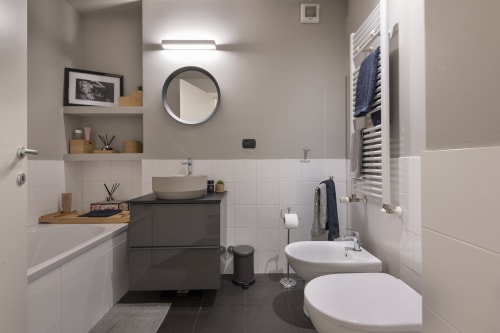 Bagno moderno della GIRESIO 41 Milan B&B con doppio lavabo, specchio tondo e rivestimento grigio-bianco