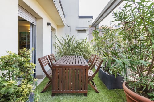 Terrazza moderna del GIRESIO 41 BnB Milano con tavolo da pranzo in legno, sedie, prato artificiale e lussureggiante vegetazione