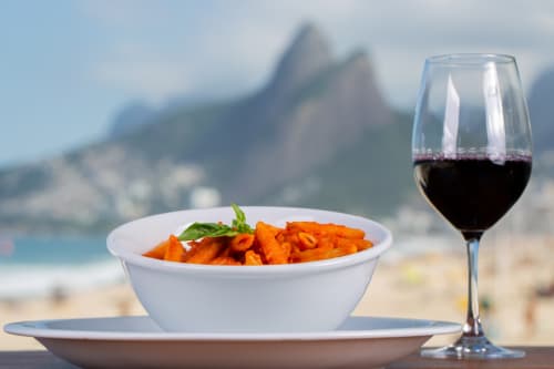 Taça de vinho tinto e prato de massa com vista para as montanhas do Rio de Janeiro na Rio Vibes Hostel