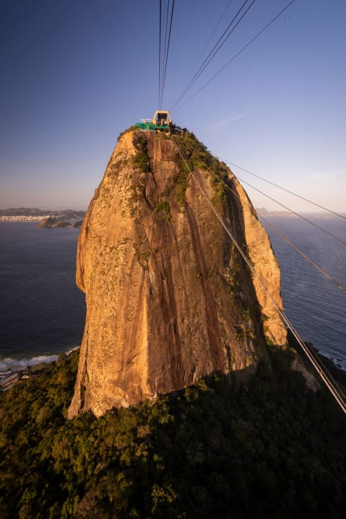 Bondinho no topo rochoso com vista para a costa do Rio de Janeiro e o oceano ao pôr do sol