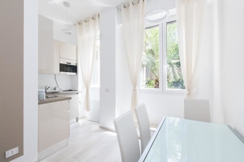 Светлая современная кухня-столовая в Magnolia Apartments Milan с белой мебелью, обеденным столом и видом на сад